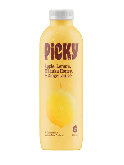 A bottle of Picky Apple, Lemon, Manuka Honey, & Ginger Juice, featuring a yellow label with a yellow pear illustration and a white cap, set against a solid pale cream background.